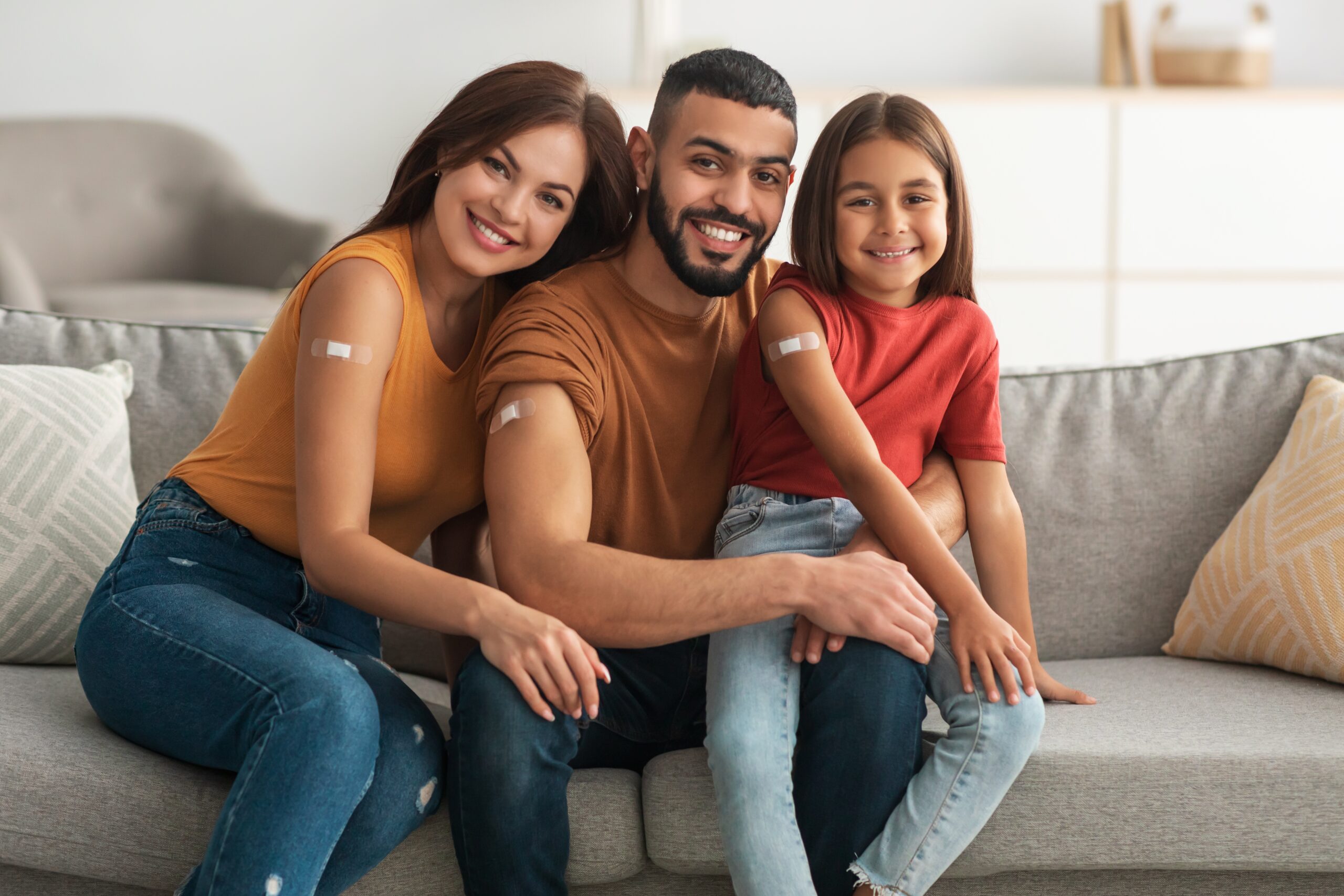 Flu Vaccine Happy Vaccinated Family Of Three People Showing Arm With Bandage After Flu Vaccine Posing Sitting On Couch In Living Room, Smiling To Camera