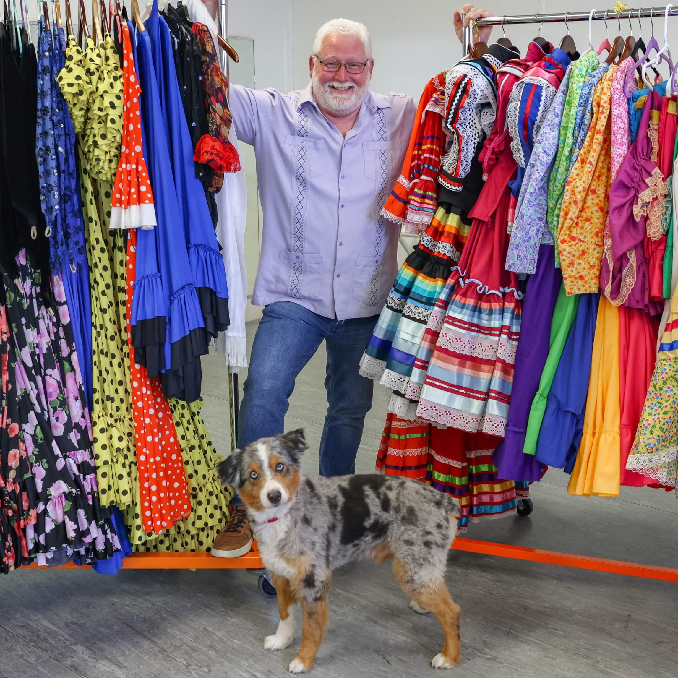 Cory Mcrae smiling with a dog stands between racks of colorful dresses.