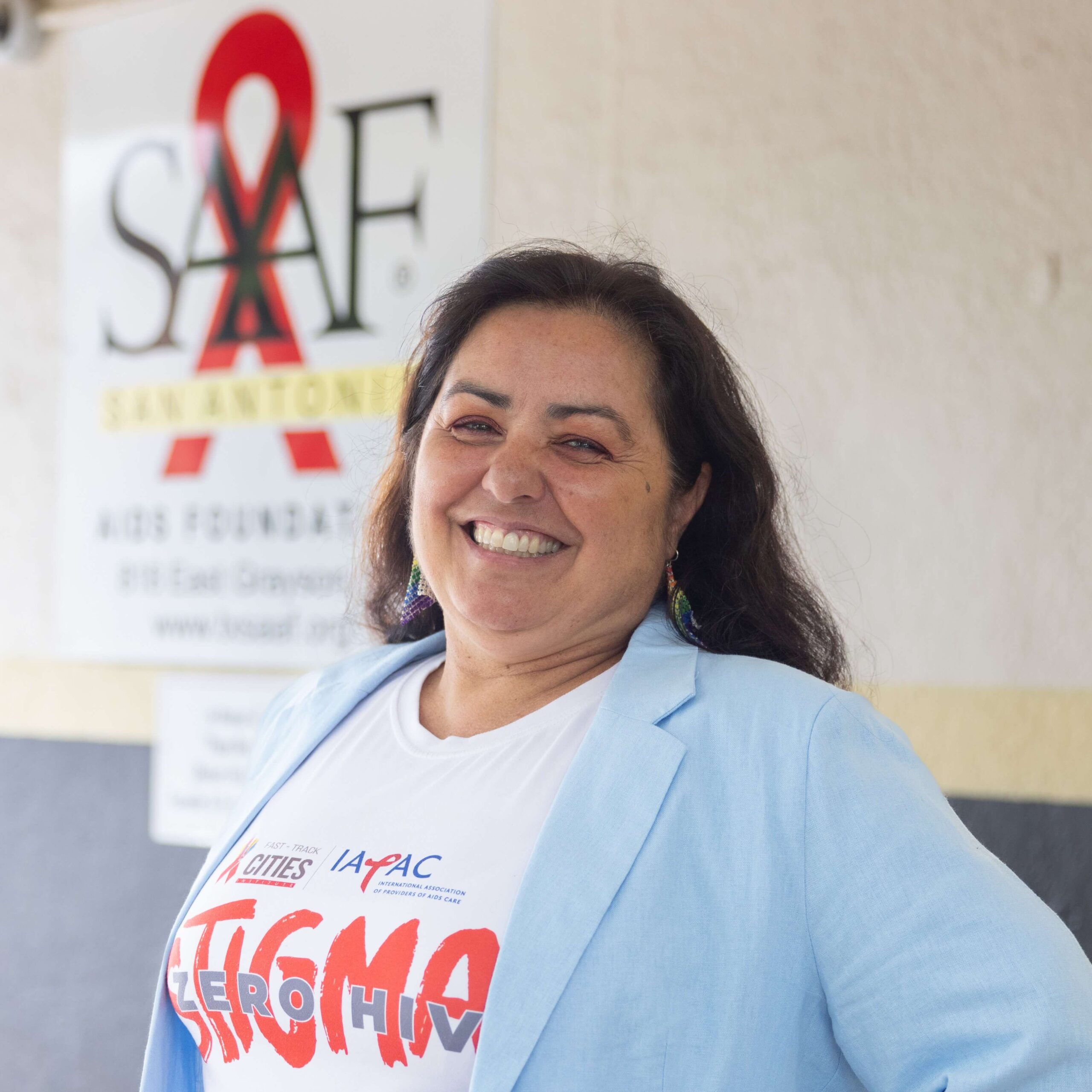 George B. Hernández Jr. wearing a blue suit and yellow tie stands in front of a screen displaying "Proud to be Local".