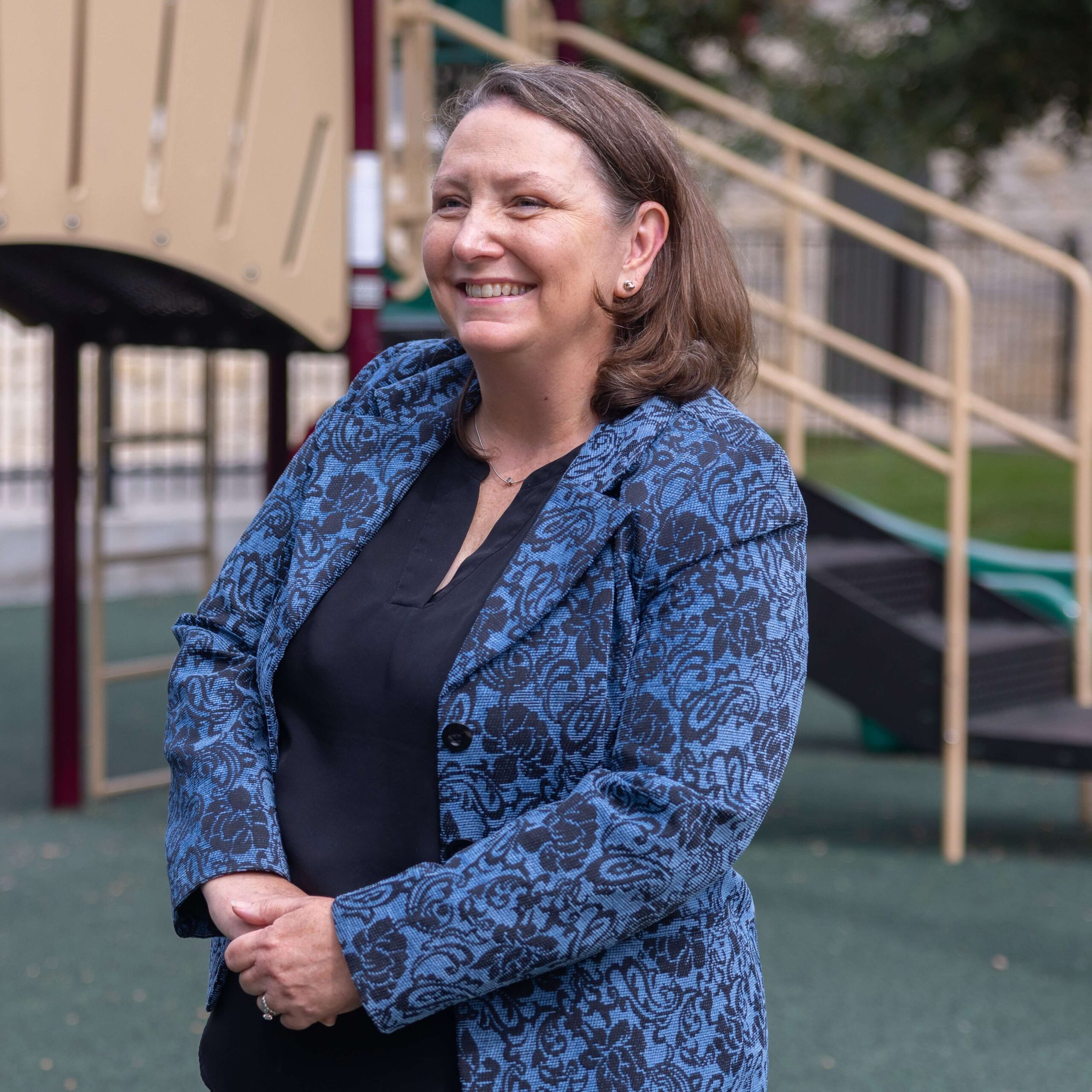 George B. Hernández Jr. wearing a blue suit and yellow tie stands in front of a screen displaying "Proud to be Local".