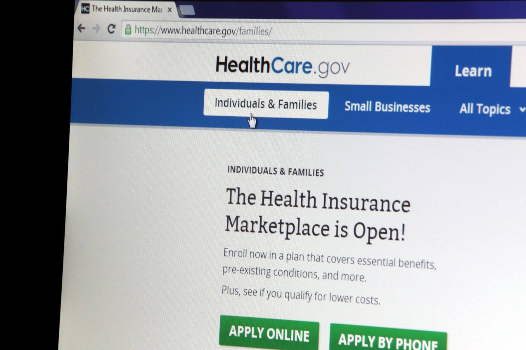 Close-up view of a computer screen displaying the HealthCare.gov website with a mouse cursor hovering over the "Individuals & Families" navigation tab.