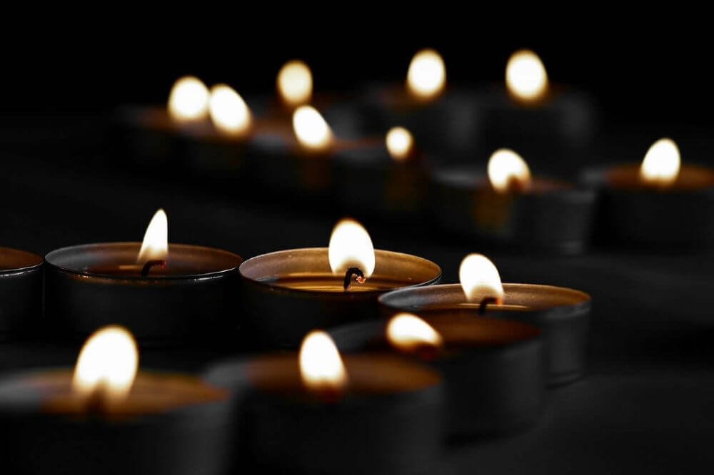 Close-up of multiple glowing tealight candles burning in darkness with shallow depth of field.