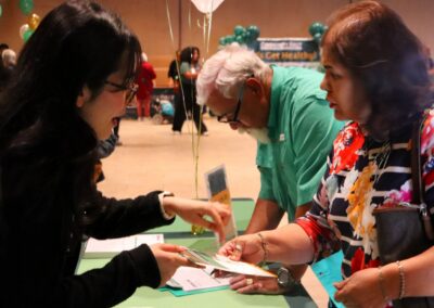 Three people are gathered around a table, looking at brochures, with balloons in the background at a "Get Healthy" event.