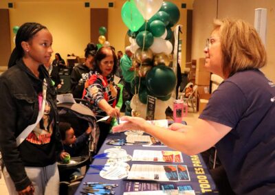 Women interact at a table with informational brochures and pens, with a balloon display in the background.