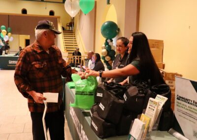 An elderly man receives a green bag from a woman at a Community First Health Plan "Let's Get Healthy" event with balloons.