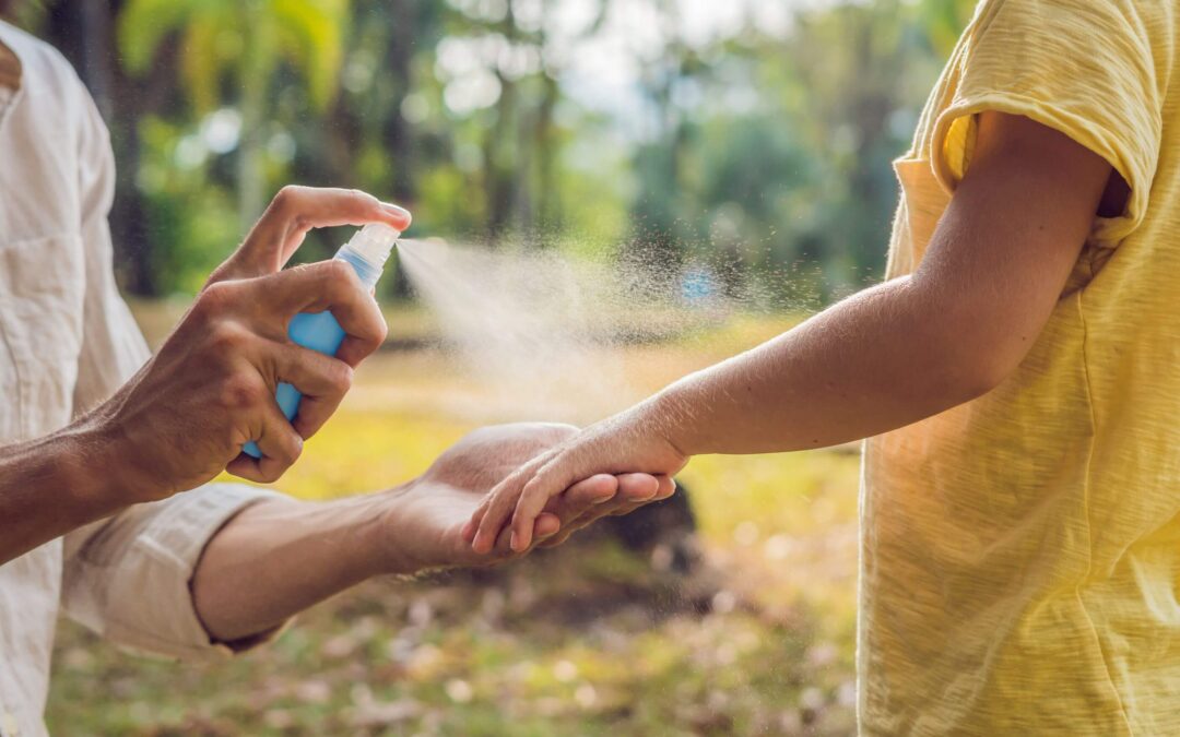 A person sprays insect repellent onto another person's arm outdoors.