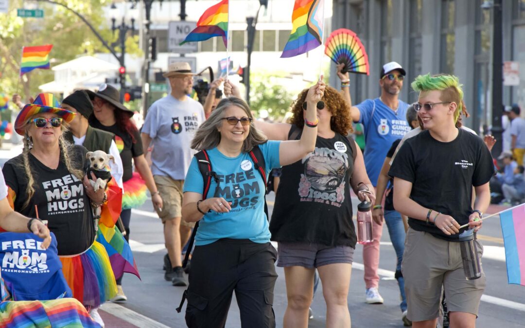 People carrying rainbow flags and fans walk in a Pride parade.