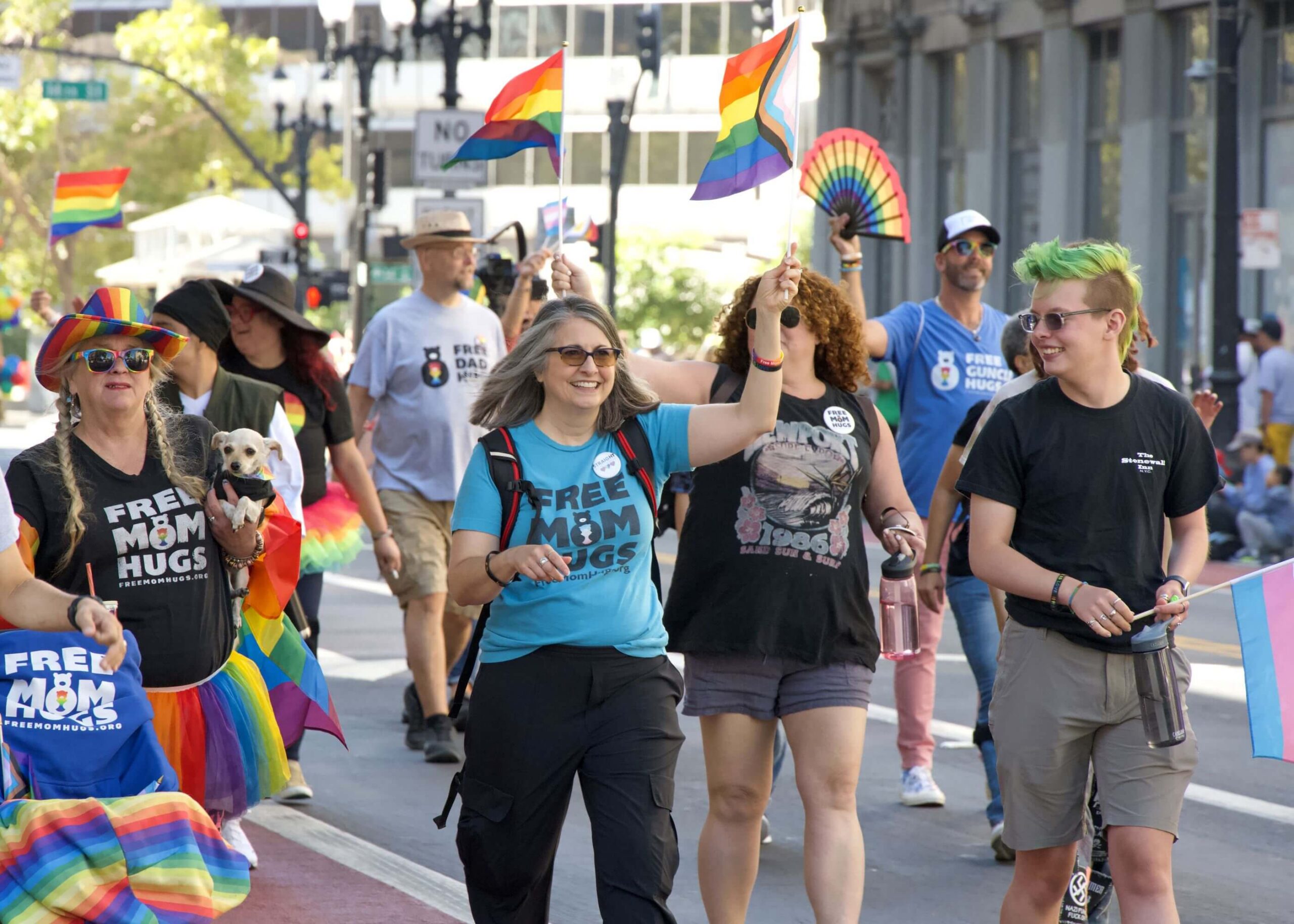 People carrying rainbow flags and fans walk in a Pride parade.
