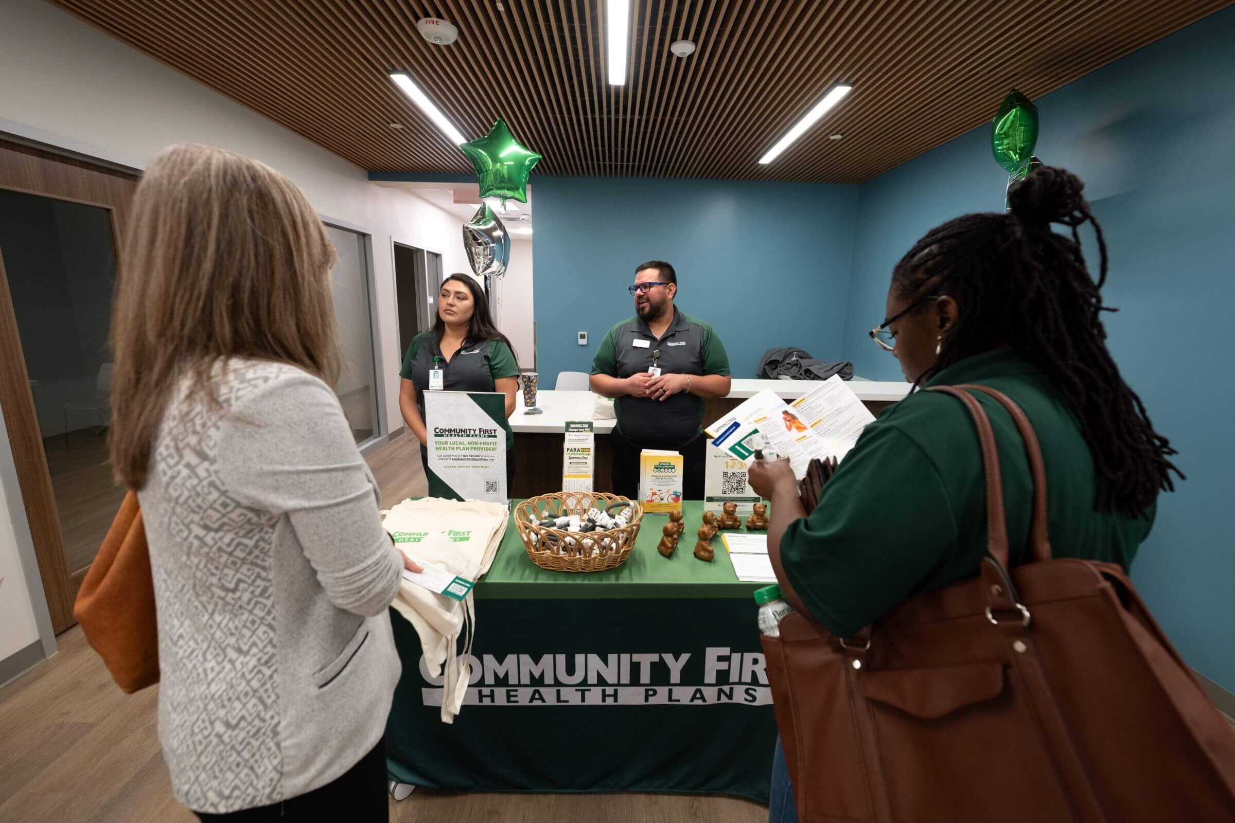 Inside of the Vida Grand Opening, two enthusiastic Community First Volunteers warmly assisting a woman, answering her questions at a Community First branded table filled with merch and informative brochures.